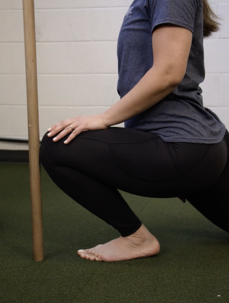 Personal trainer demonstrating the kneeling ankle dorsiflexion test to assess ankle mobility and squat readiness.